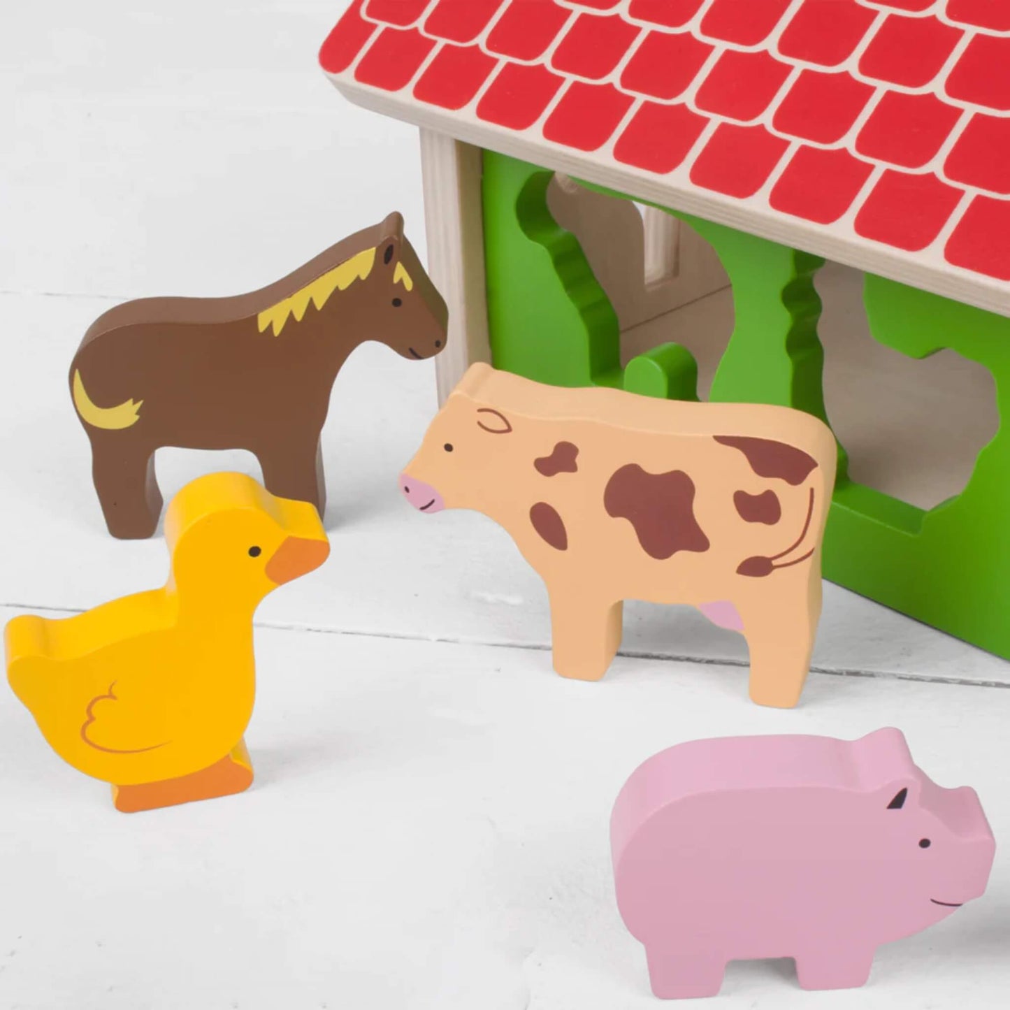 Close-up of wooden farm animals, including a yellow duck, brown horse, pink pig, and cream cow with brown patches, ready for sorting.