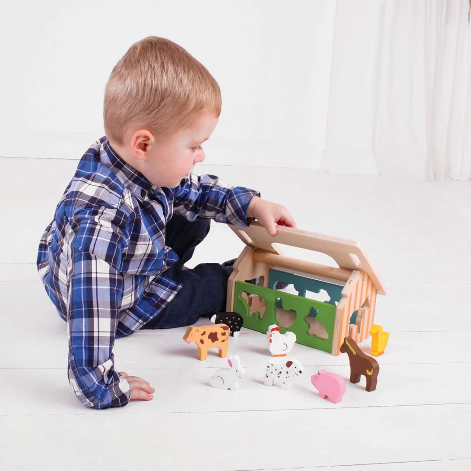 Young child playing with a wooden farmhouse shape sorter, exploring the chunky animal pieces and fitting them into the matching slots – a hands-on way to learn about shapes and animals.