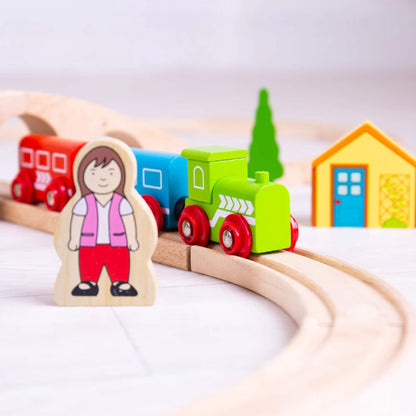 Wooden figure of a woman next to the train track with a blue and red carriage and engine passing behind.