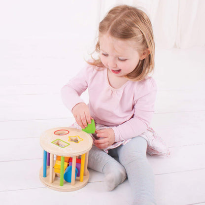 Smiling child placing a green square into the wooden rolling shape sorter, developing hand-eye coordination and fine motor skills.