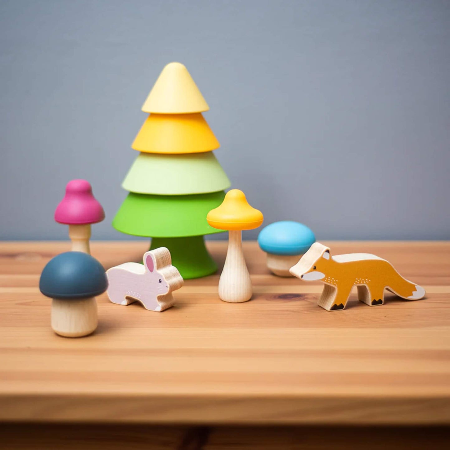 A styled tabletop scene with the Bigjigs Toys Forest Friends Playset, showing the tree, bunny, fox, and mushrooms against a wooden background.