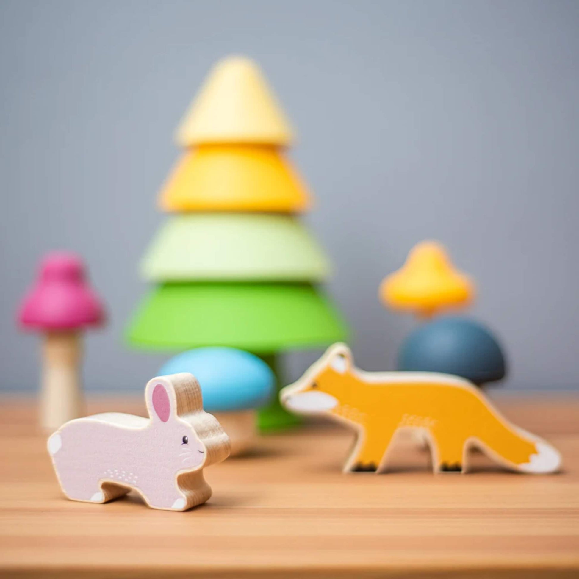 A close-up of the Forest Friends Playset, showing a yellow and green stacking tree, wooden bunny, fox, and four silicone mushrooms in assorted colours.