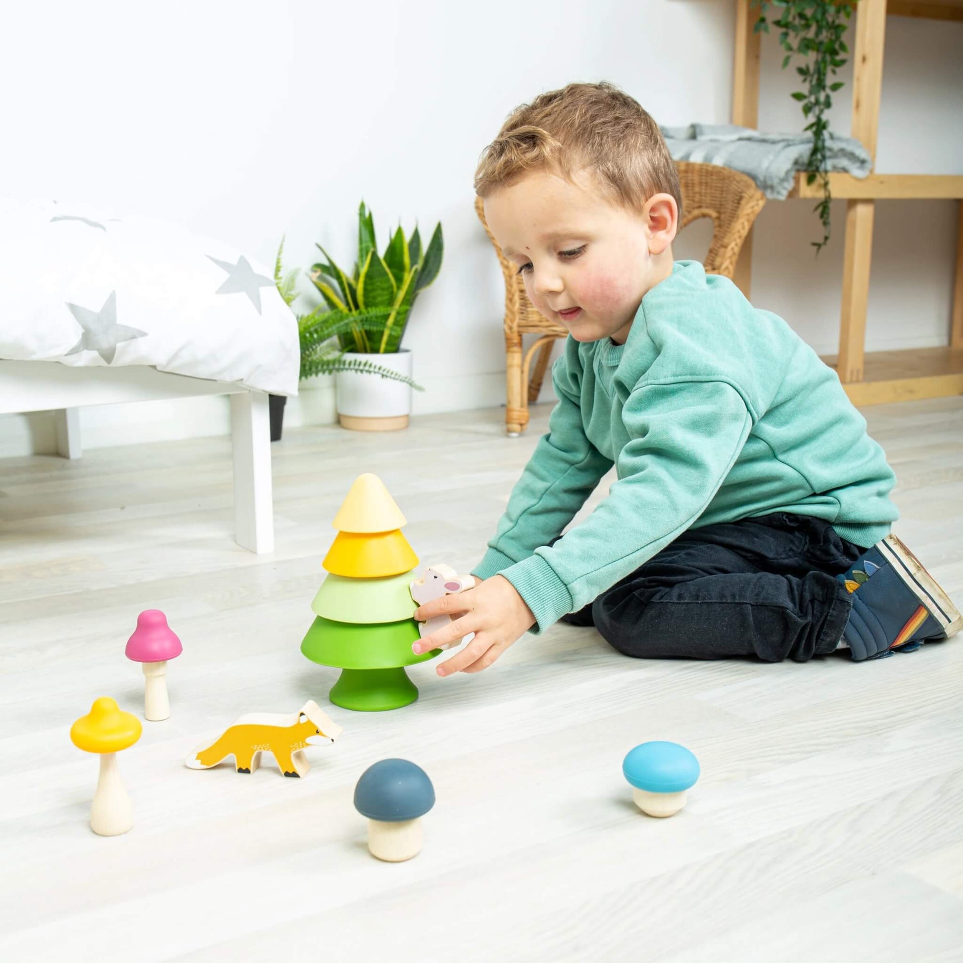 A young child placing the bunny figure near the stacking tree from the Forest Friends Playset, surrounded by silicone mushrooms.