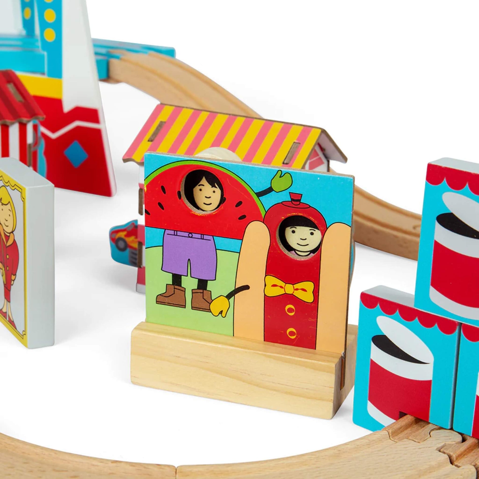 Colourful wooden fairground cut-out board with holes for faces, showing watermelon and hotdog characters with peeking wooden heads.