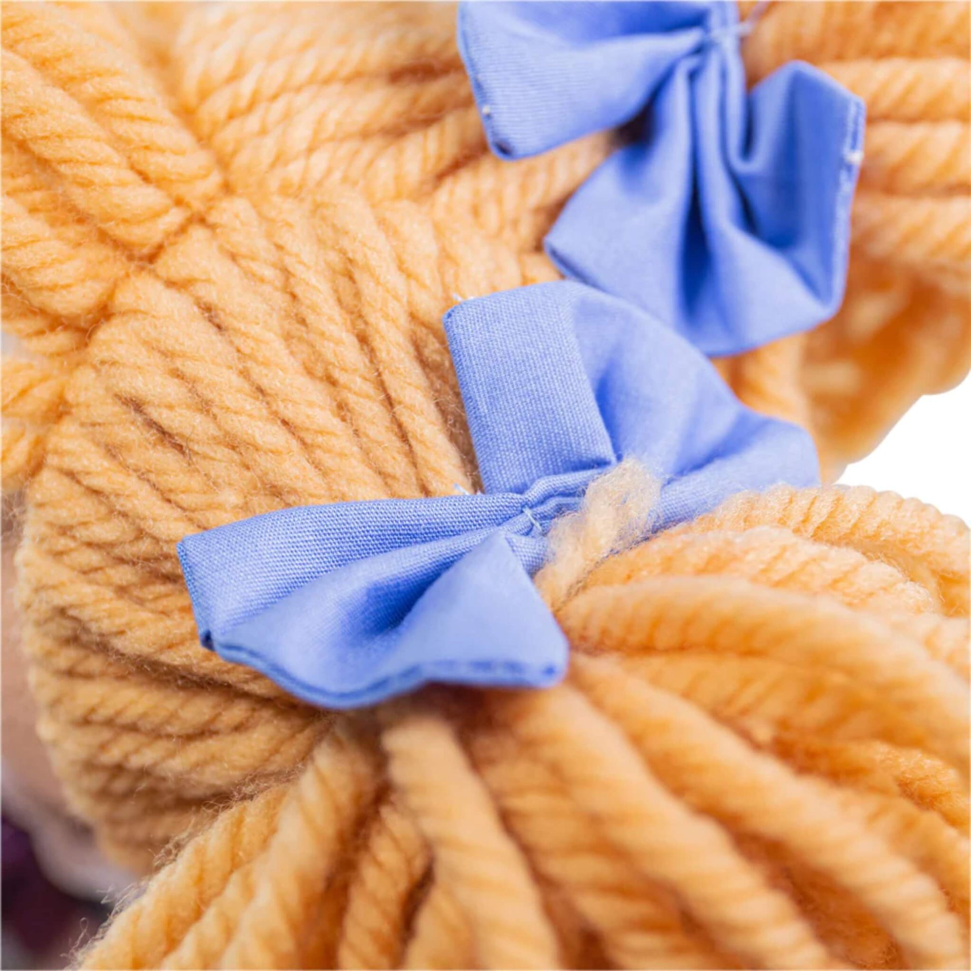 Detailed image of the soft blonde yarn hair tied with two neat blue fabric bows on Katie Doll’s pigtails.