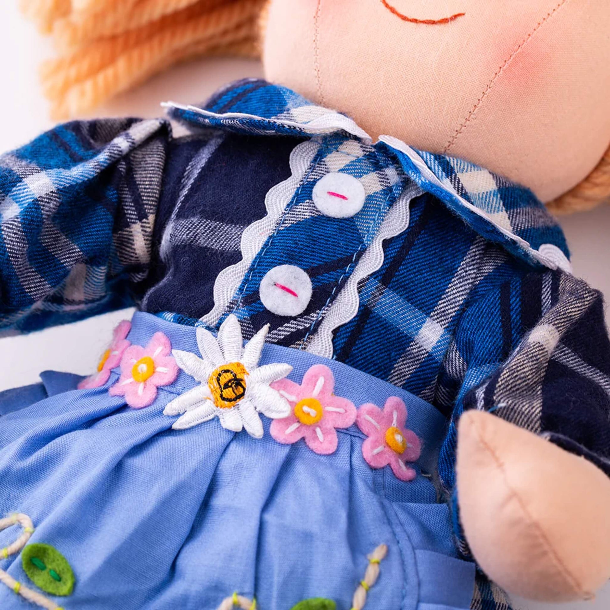 Embroidery detail – Close-up of Katie Doll’s apron belt showing embroidered daisies and a bee with pink and yellow flower accents.