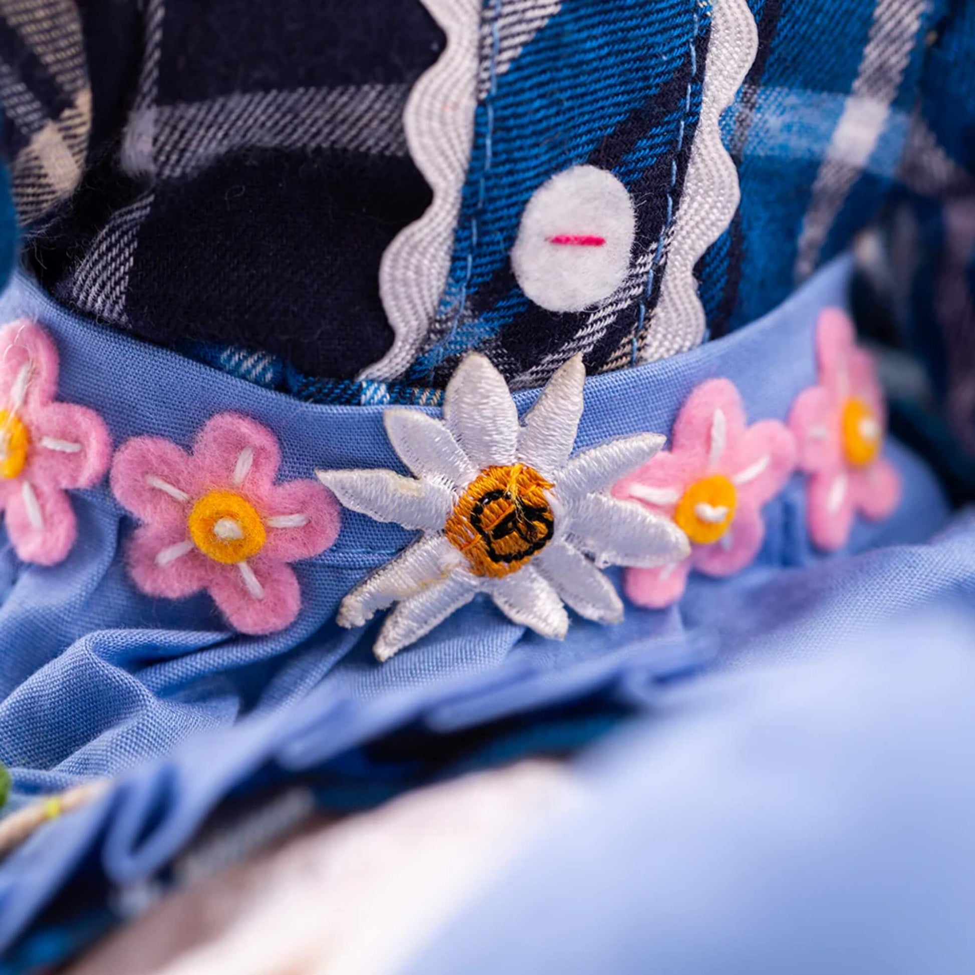 Bee and flower embroidery close-up – Zoomed-in embroidery of a white daisy and pink flowers stitched on the blue apron of Katie Doll.
