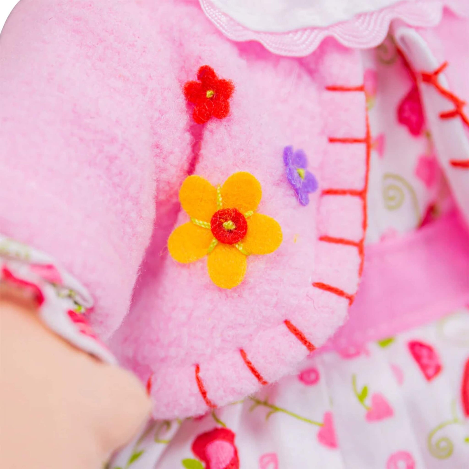 Embroidered yellow, red, and purple flowers stitched onto pink felt cardigan with blanket stitch edging.