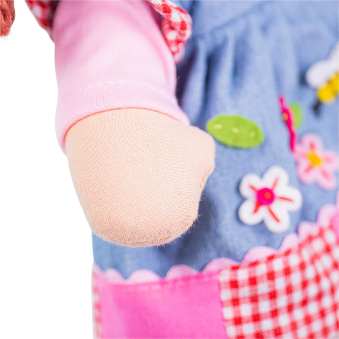 Close-up of the doll’s soft arm and sleeve, with pink cuff and floral skirt embroidery visible in the background.