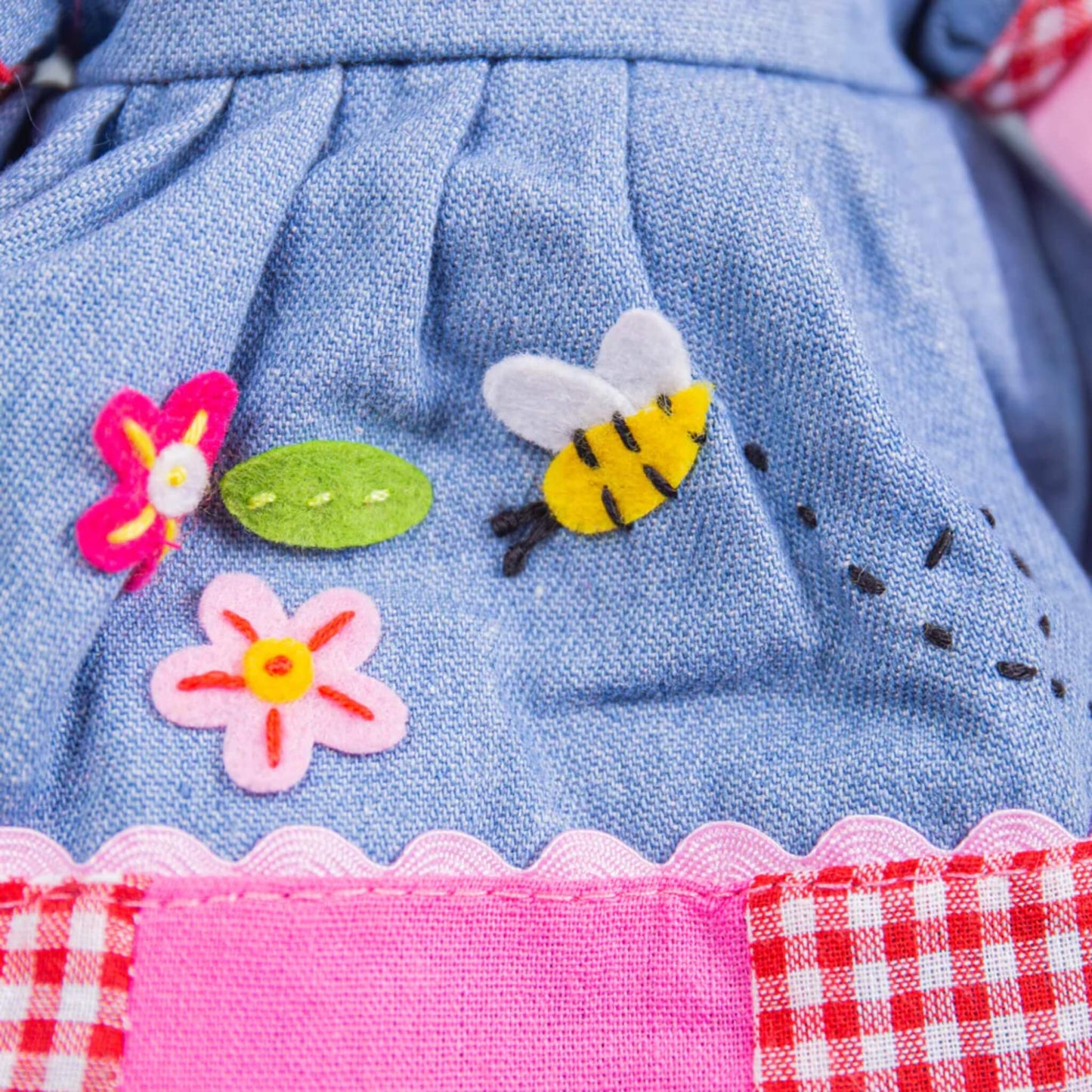 Close-up of felt bee and flower appliqués stitched to the front of the dress, with visible stitching on soft blue fabric.