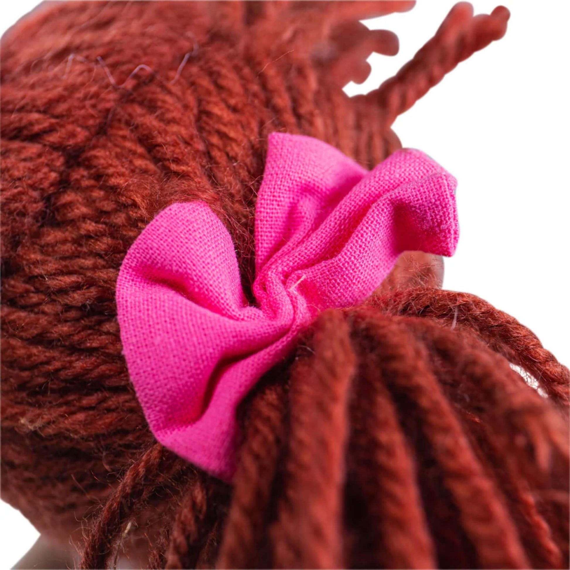 View of the bright pink bow tied into Melody Doll’s auburn yarn hair.