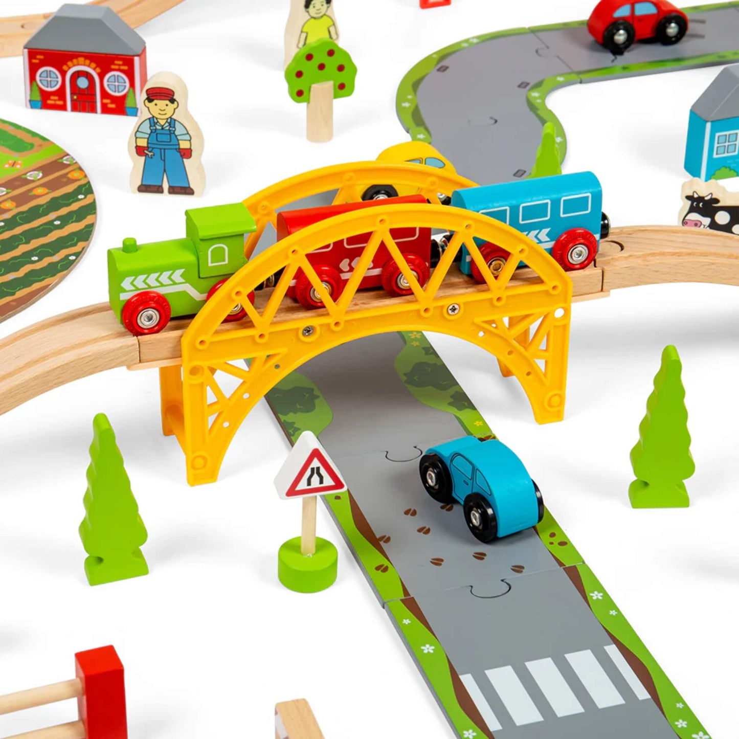 Close-up of the yellow plastic bridge from the Road and Rail Train Set with a wooden train passing overhead and a blue toy car driving underneath on the painted road.