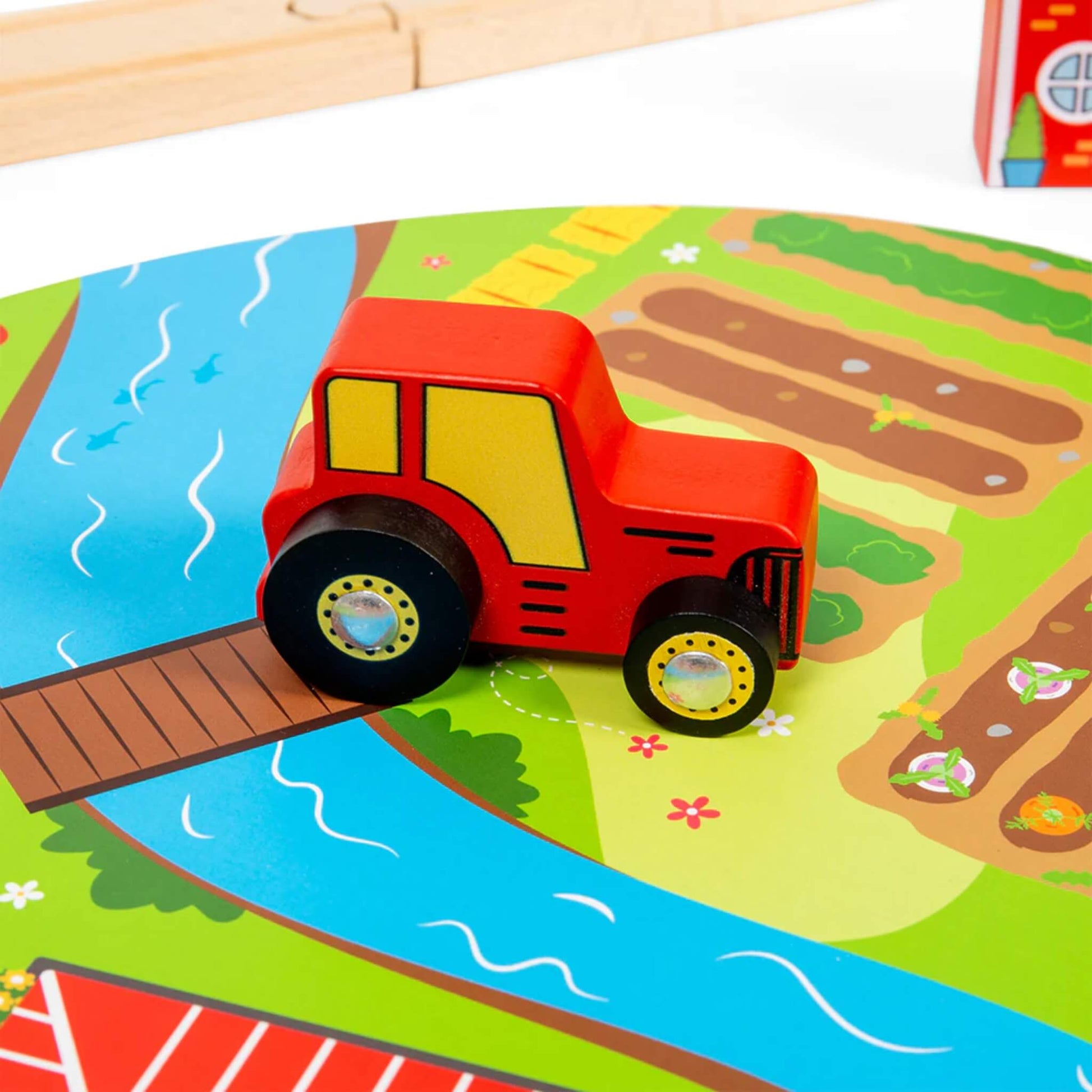 Close-up of the red tractor on the illustrated farm play mat, which features a winding river, fields, and bright flowers.
