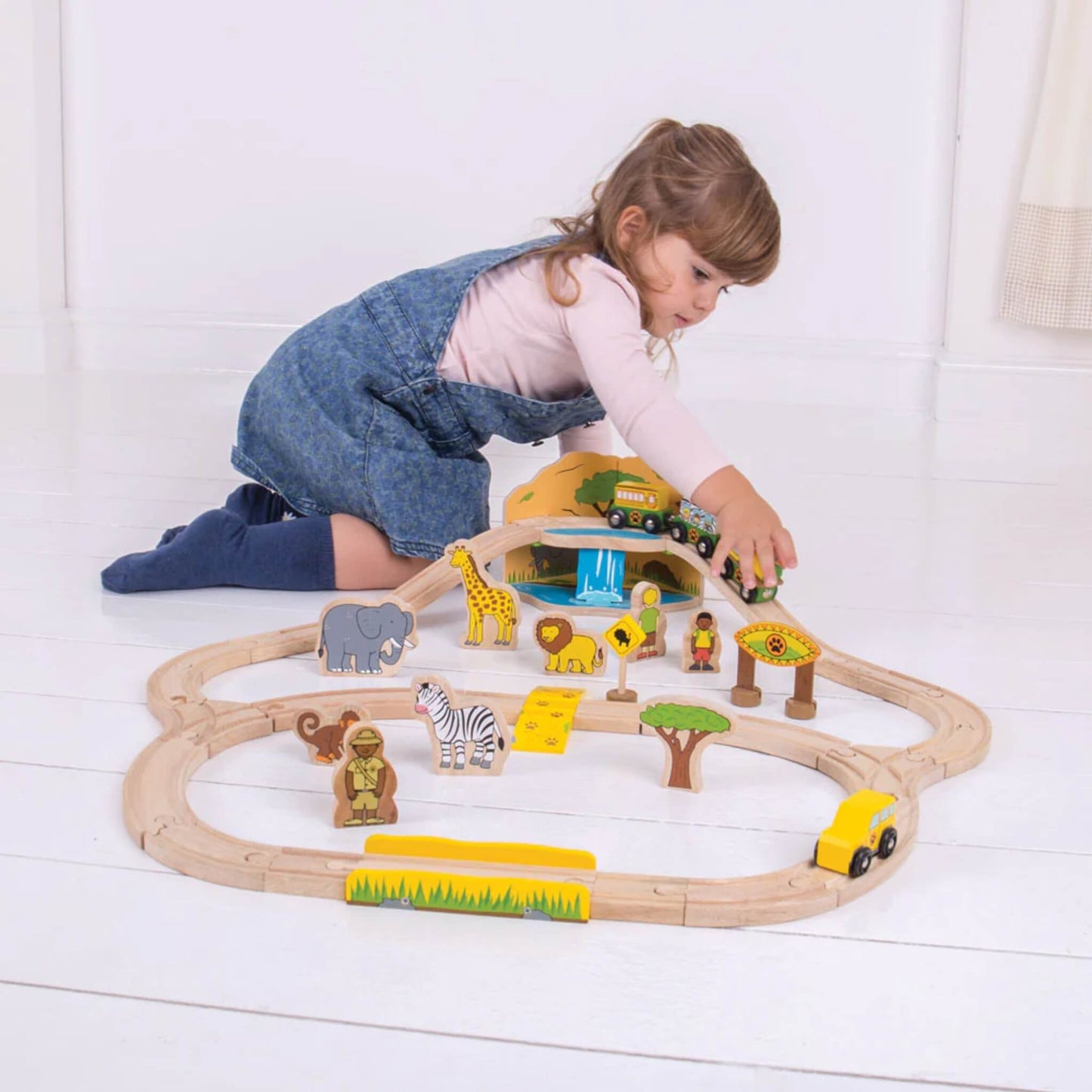 Girl reaching to guide the safari train set around the upper level of the wooden bridge with the animals below.