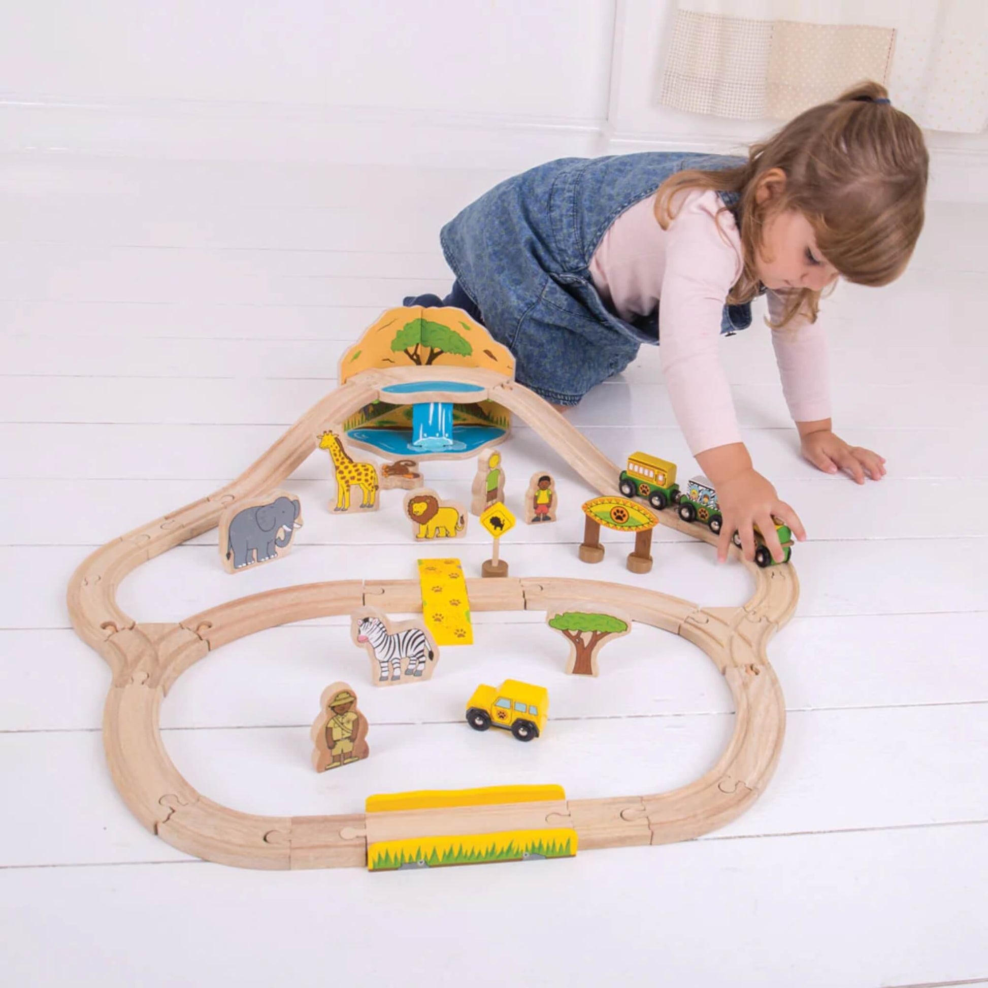 Overhead view of a young child interacting with the complete wooden safari train layout on the floor.