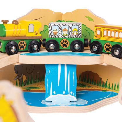 View of the train travelling across the bridge section of the set, showing safari passengers painted on the carriage above a blue waterfall backdrop.
