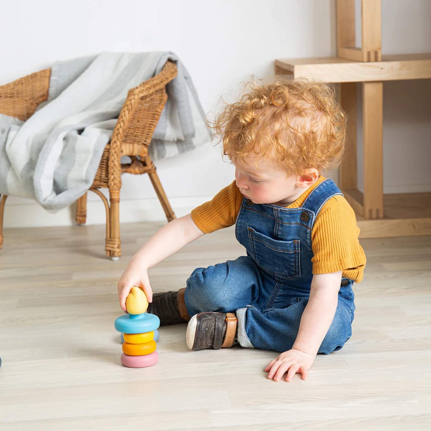 A young child playing on a light floor, carefully placing a ring onto the Bigjigs Toys Silicone Stacking Cat toy, surrounded by neutral home décor.