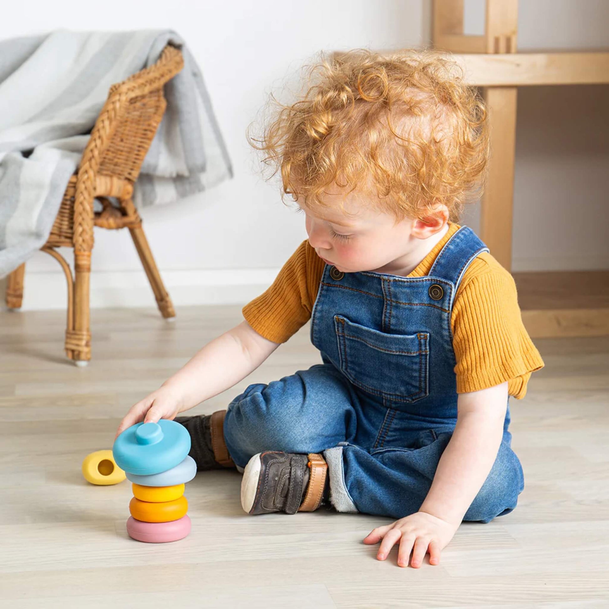 Child sitting cross-legged, stacking pastel and primary-coloured rings onto the Bigjigs Toys Silicone Cat Stacker, fully engaged in play.