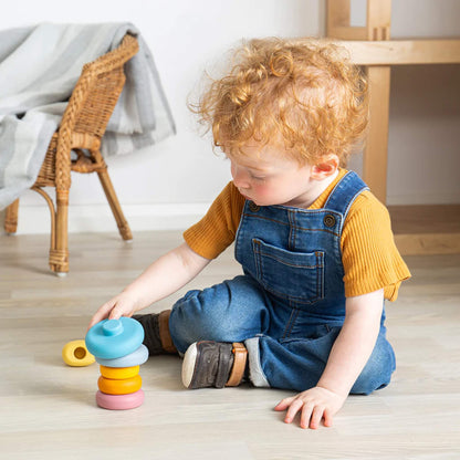 Child sitting cross-legged, stacking pastel and primary-coloured rings onto the Bigjigs Toys Silicone Cat Stacker, fully engaged in play.