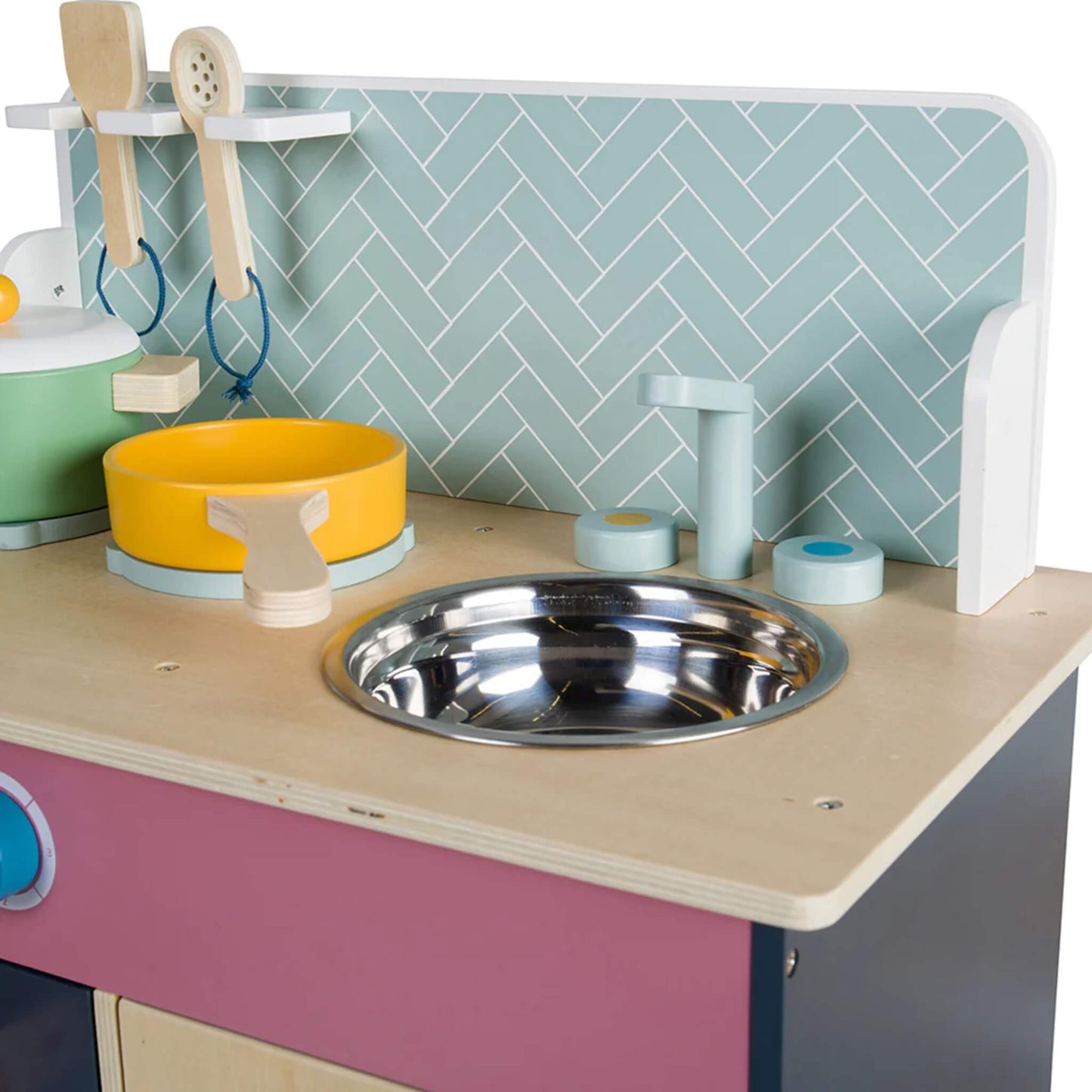 Close-up of the toy sink area with wooden taps and a metal bowl, set against a pale green herringbone splashback.