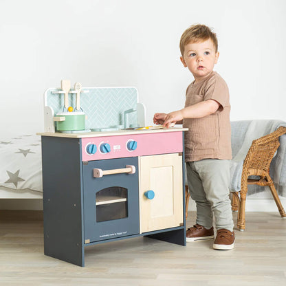 Toddler playing beside the Simply Scandi Kitchen, reaching for a utensil while engaging in pretend cooking play.