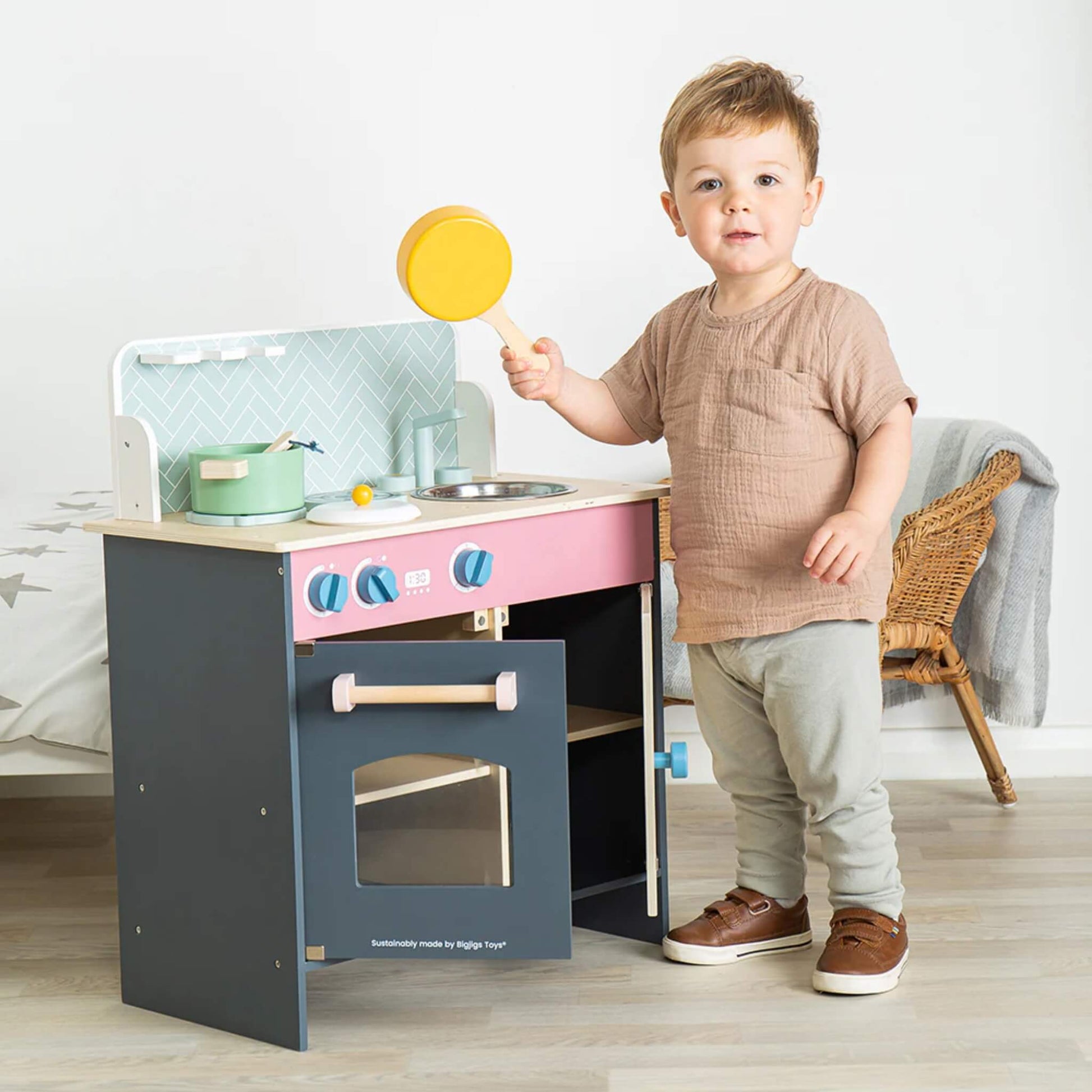 Child holding a yellow wooden frying pan next to the Simply Scandi Kitchen, smiling at the camera.