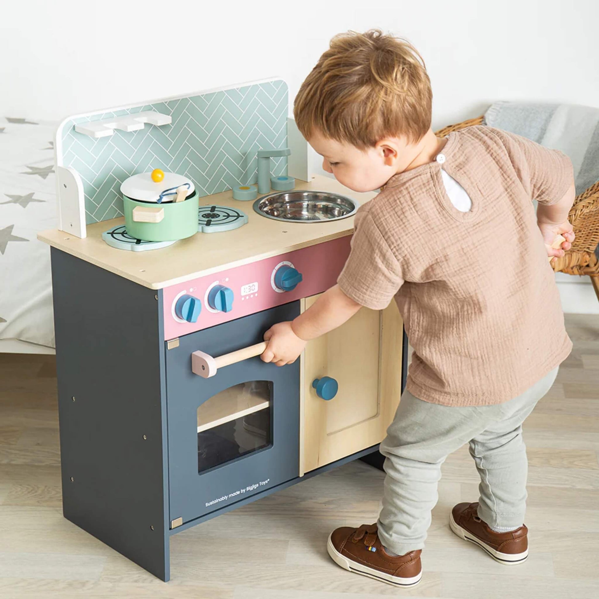 Little boy interacting with the oven door on the Bigjigs kitchen set, demonstrating open-ended play features.