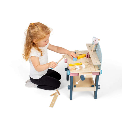 Young girl playfully using the wooden hammer and other tools on the Bigjigs Tool Bench, surrounded by pieces.