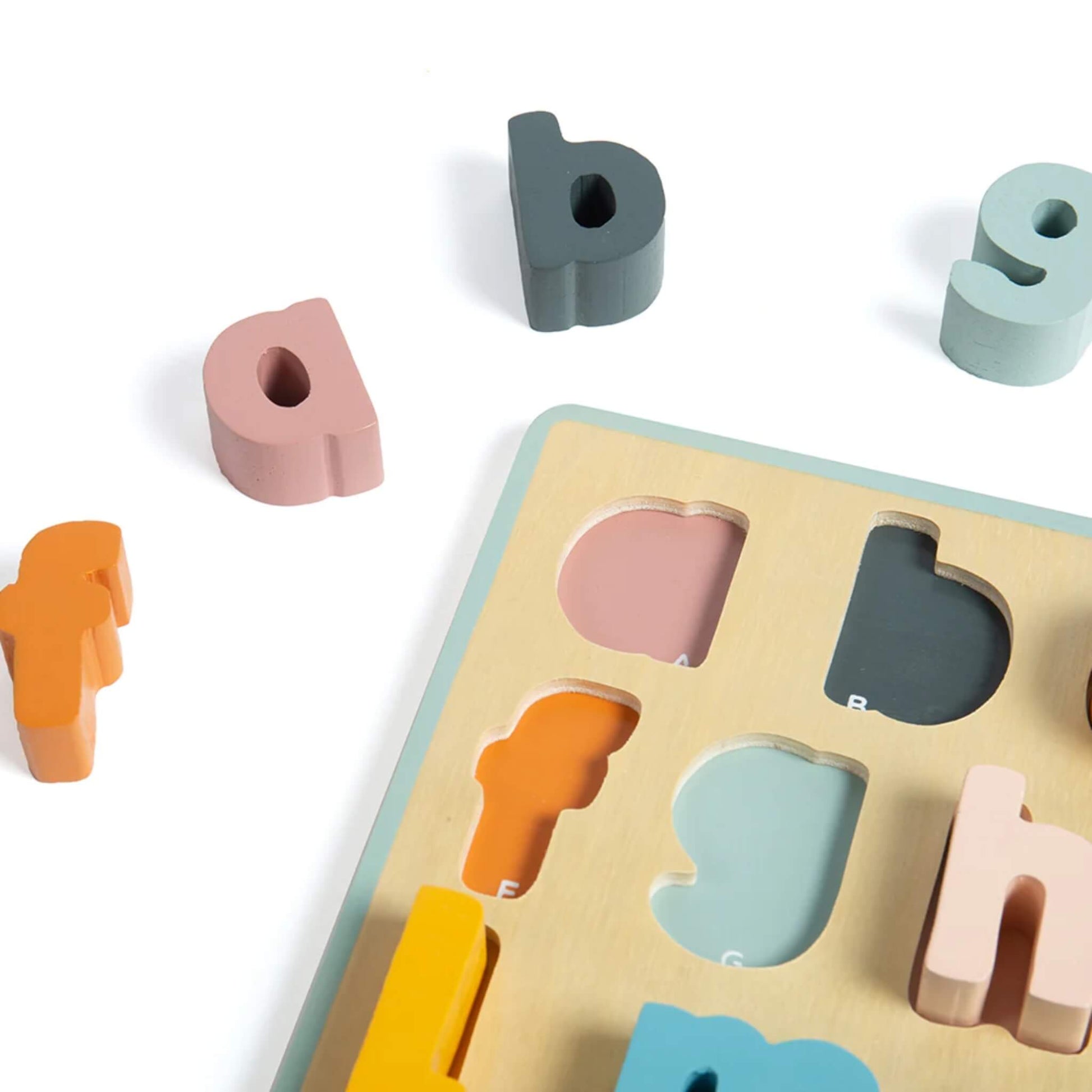 Close-up of pastel wooden lowercase letters on the alphabet puzzle, showing matching slots and bright, child-friendly colours.
