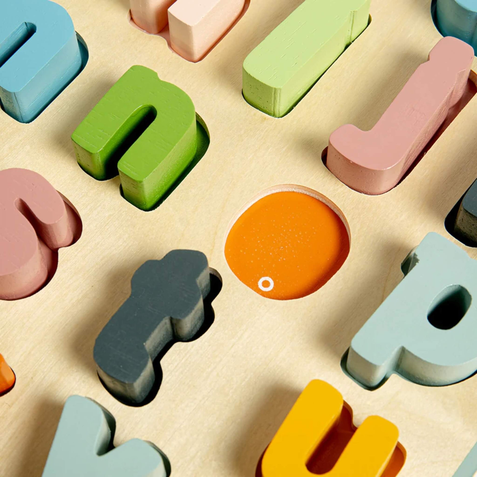 Close-up of wooden lower case letter fitting into their matching slots, highlighting the colour-matching design.