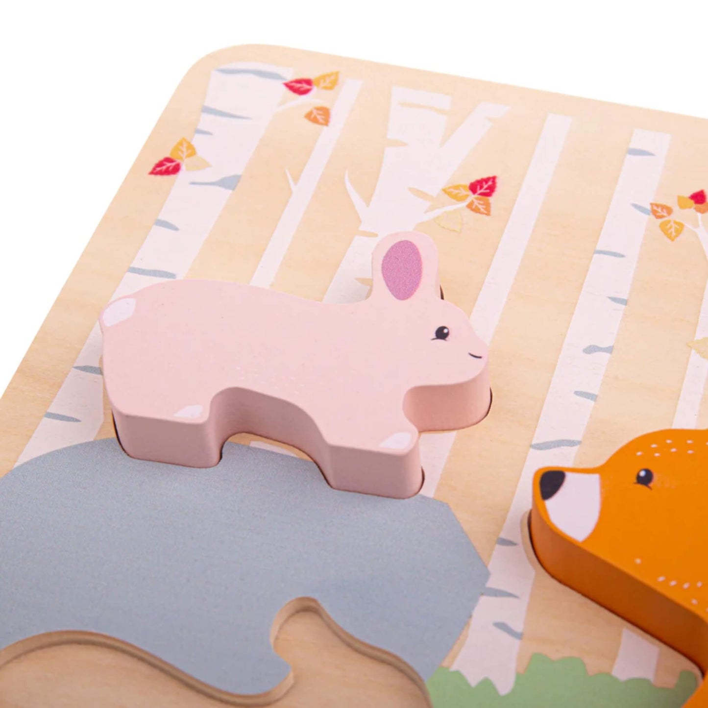 Close-up of a pink wooden rabbit puzzle piece being placed into its matching slot on a woodland-themed board, with birch trees and autumn leaves in the background.