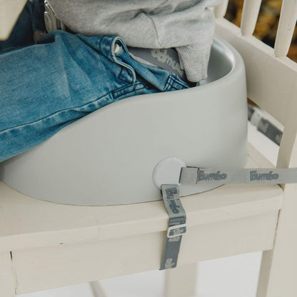 Close-up of the Bumbo Booster Seat in Cool Grey secured to a wooden dining chair with adjustable straps.