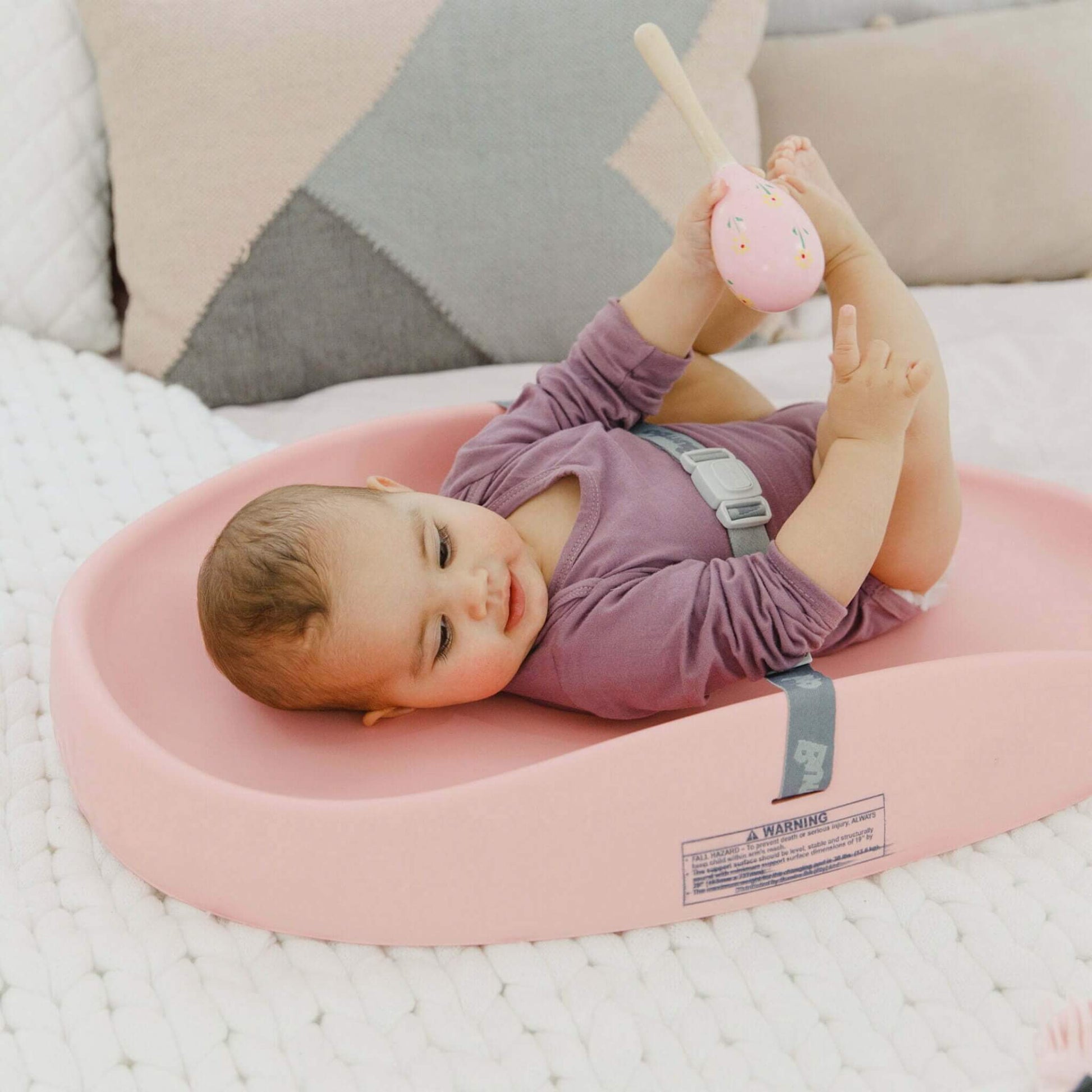 Baby playing happily on Bumbo Cradle Pink Changing Pad with toy.