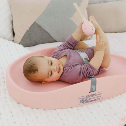 Baby playing happily on Bumbo Cradle Pink Changing Pad with toy.