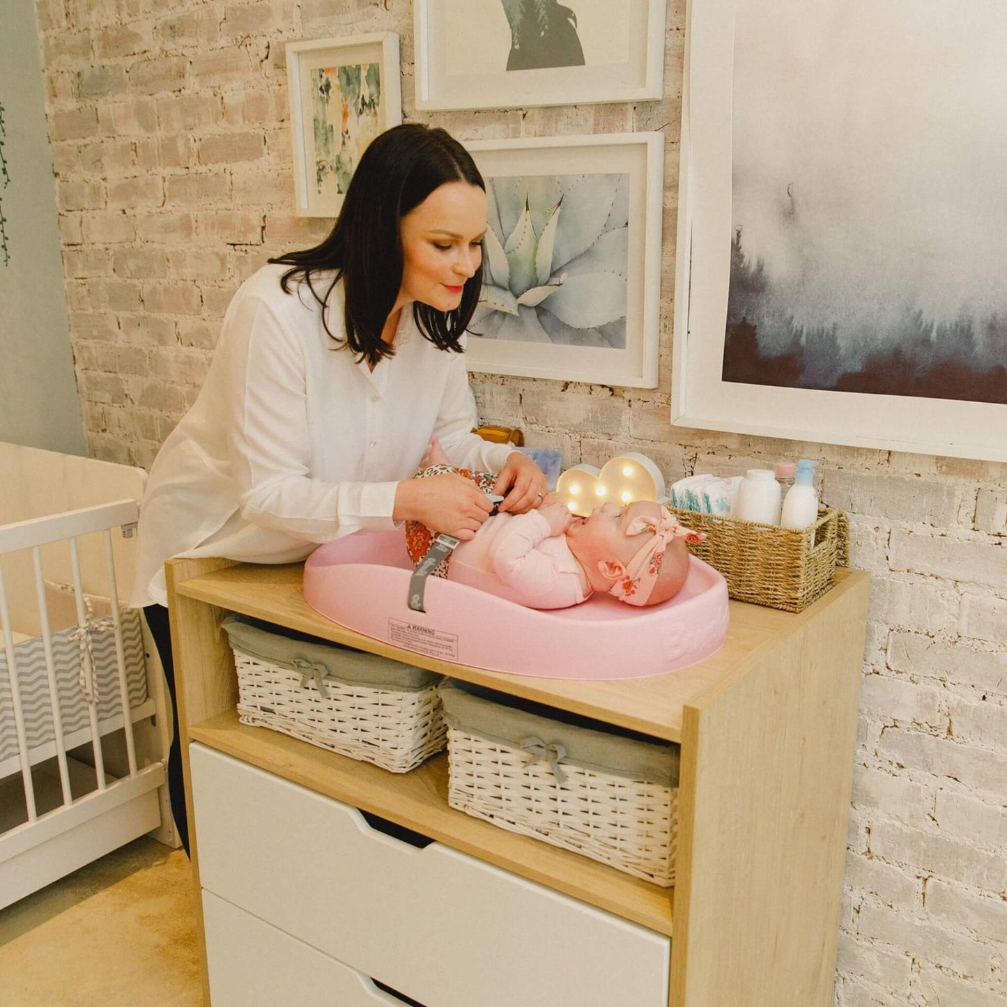Mother changing baby on Bumbo Cradle Pink Changing Pad in nursery.