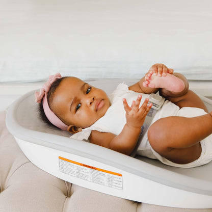 Baby lying comfortably on the Bumbo Max Changing Pad in Cool Grey, placed on a cushioned ottoman.