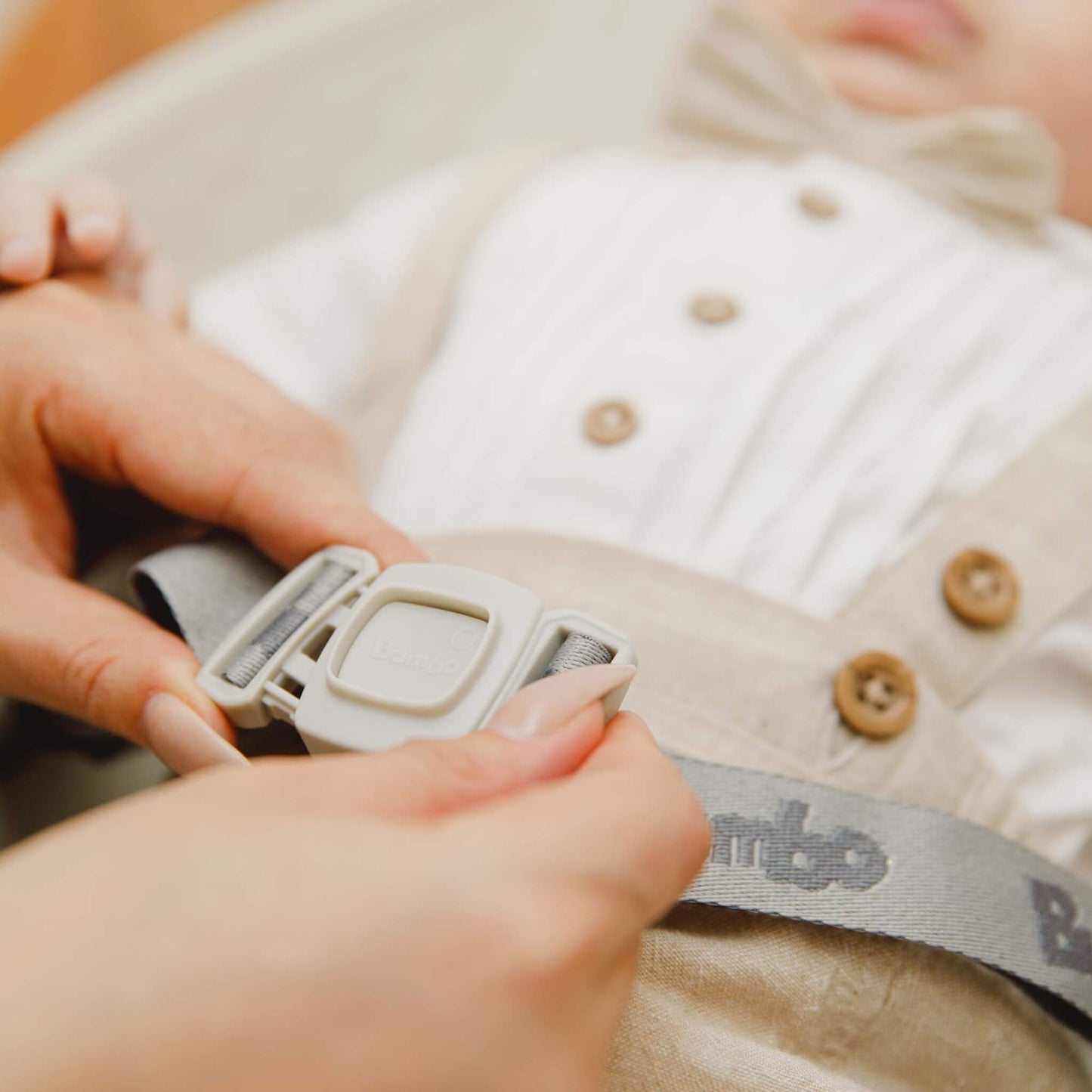 Close-up of a parent fastening the safety harness on the Bumbo Max Changing Pad in Taupe.