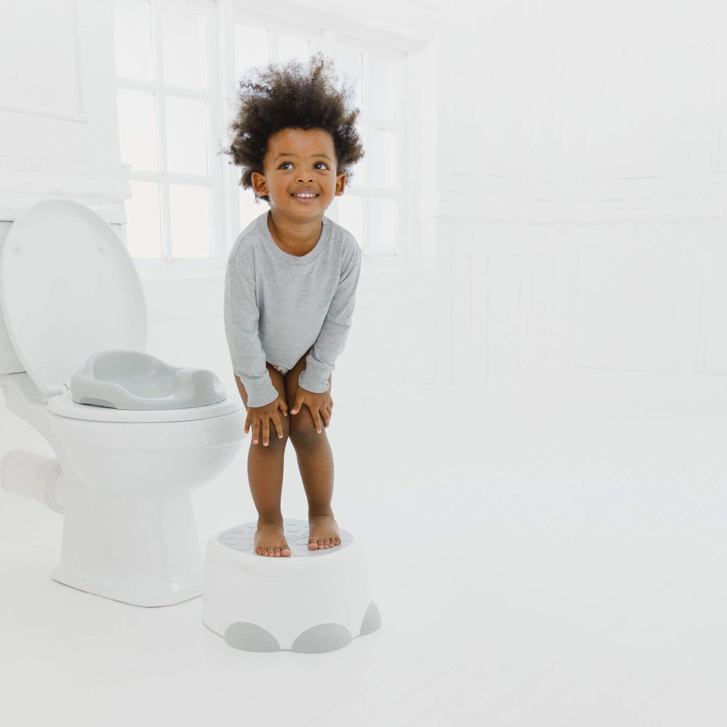 Toddler using Bumbo Step ‘n Potty as a step stool next to a toilet.