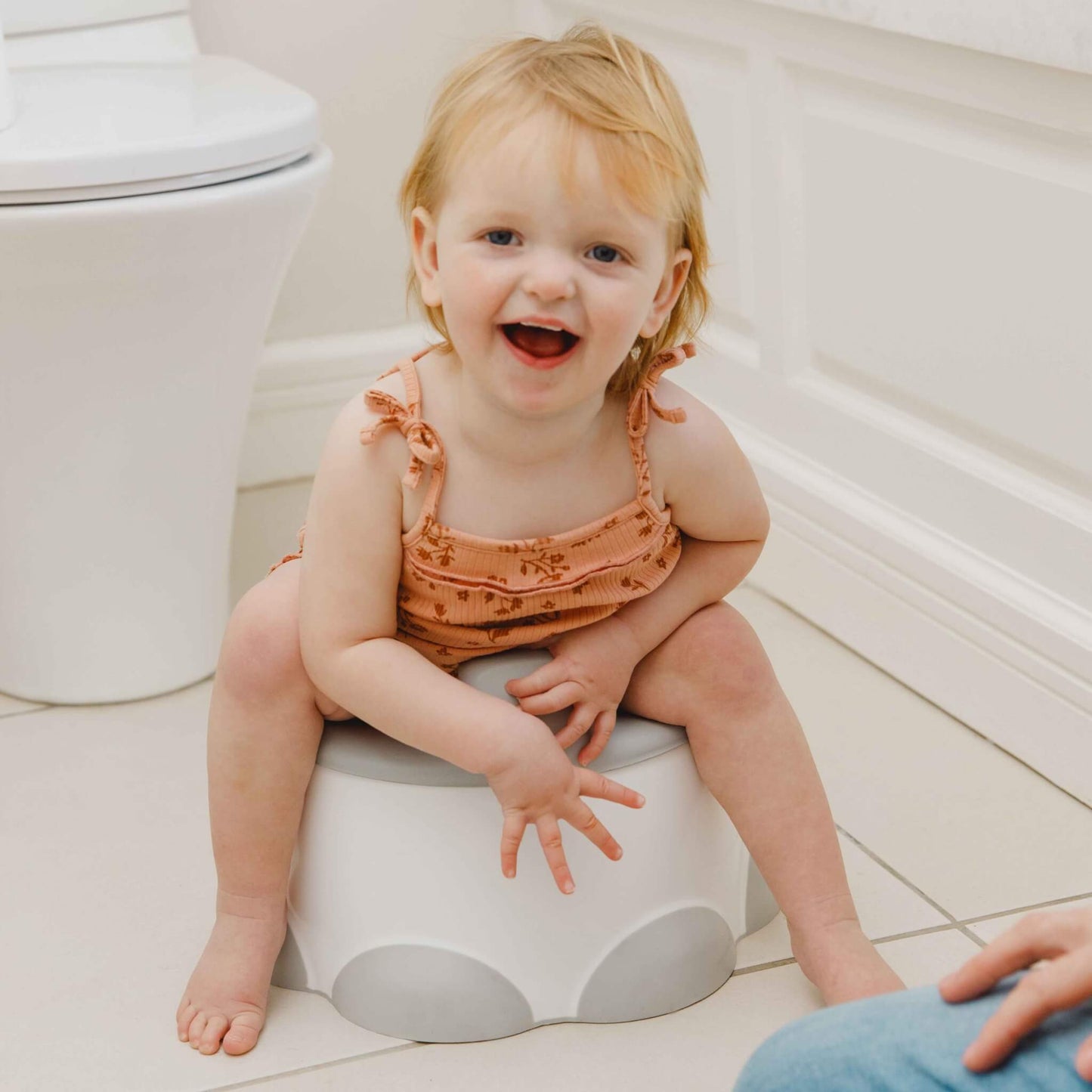 Smiling toddler sitting comfortably on Bumbo Step ‘n Potty in bathroom.