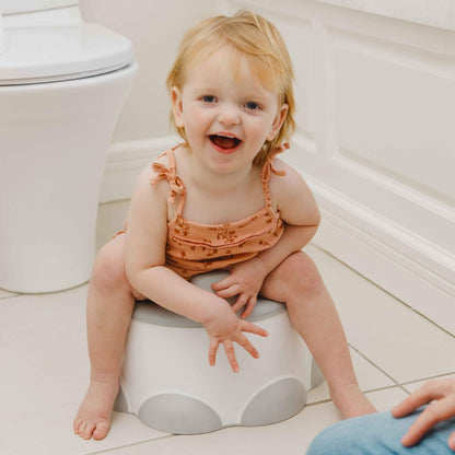 Smiling toddler sitting comfortably on Bumbo Step ‘n Potty in bathroom.