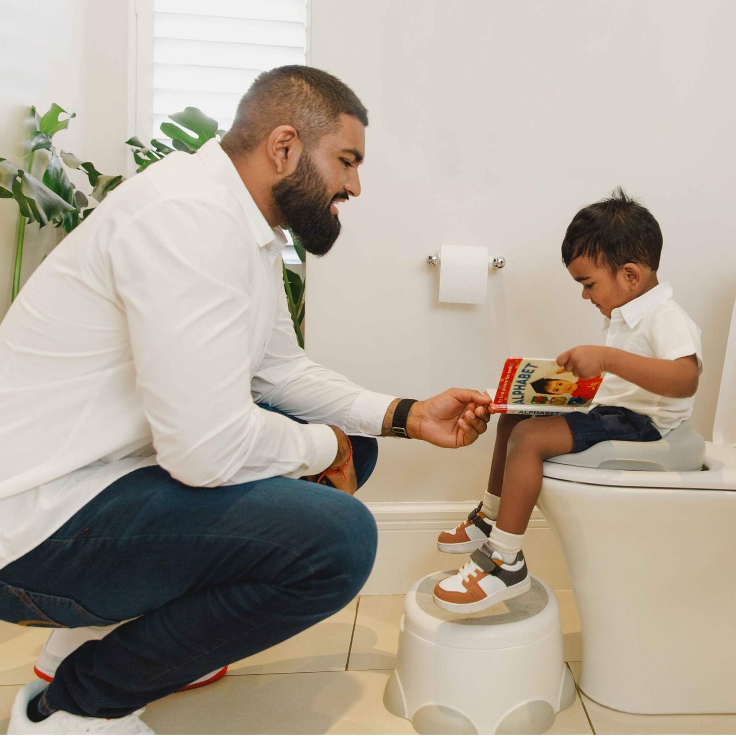 Father helping toddler use toilet with Bumbo Step ‘n Potty as a step.