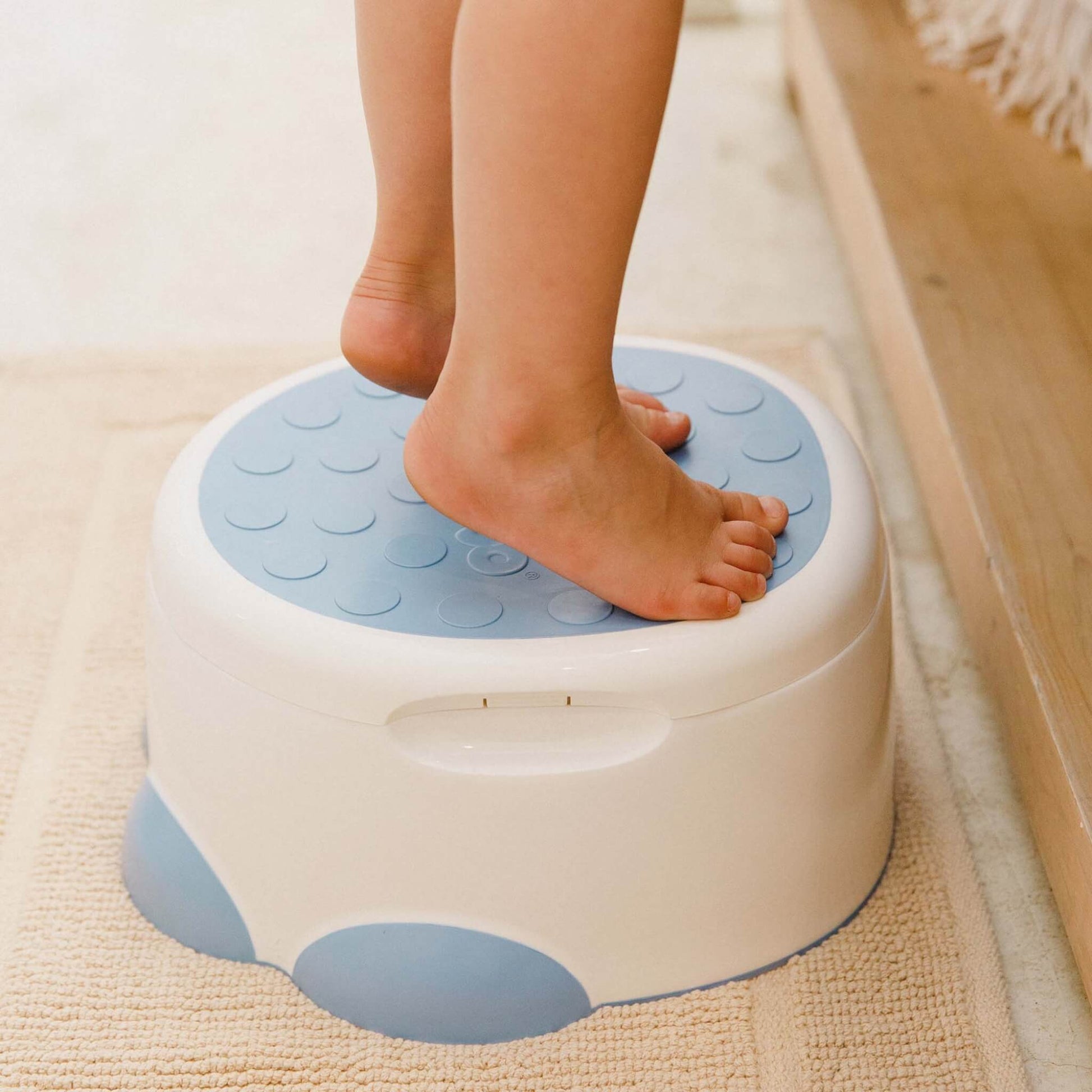 Child’s feet standing on the non-slip top of the Bumbo Step ‘n Potty in Powder Blue.