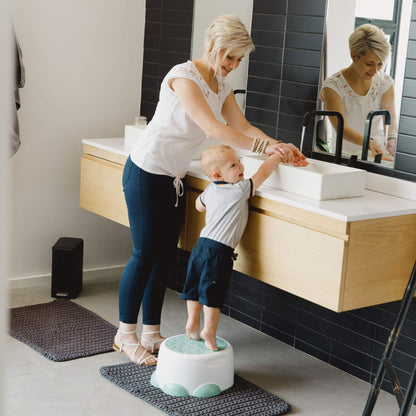 Toddler standing on the Step 'n Potty at a sink while washing hands with an adult, showcasing stool mode use.