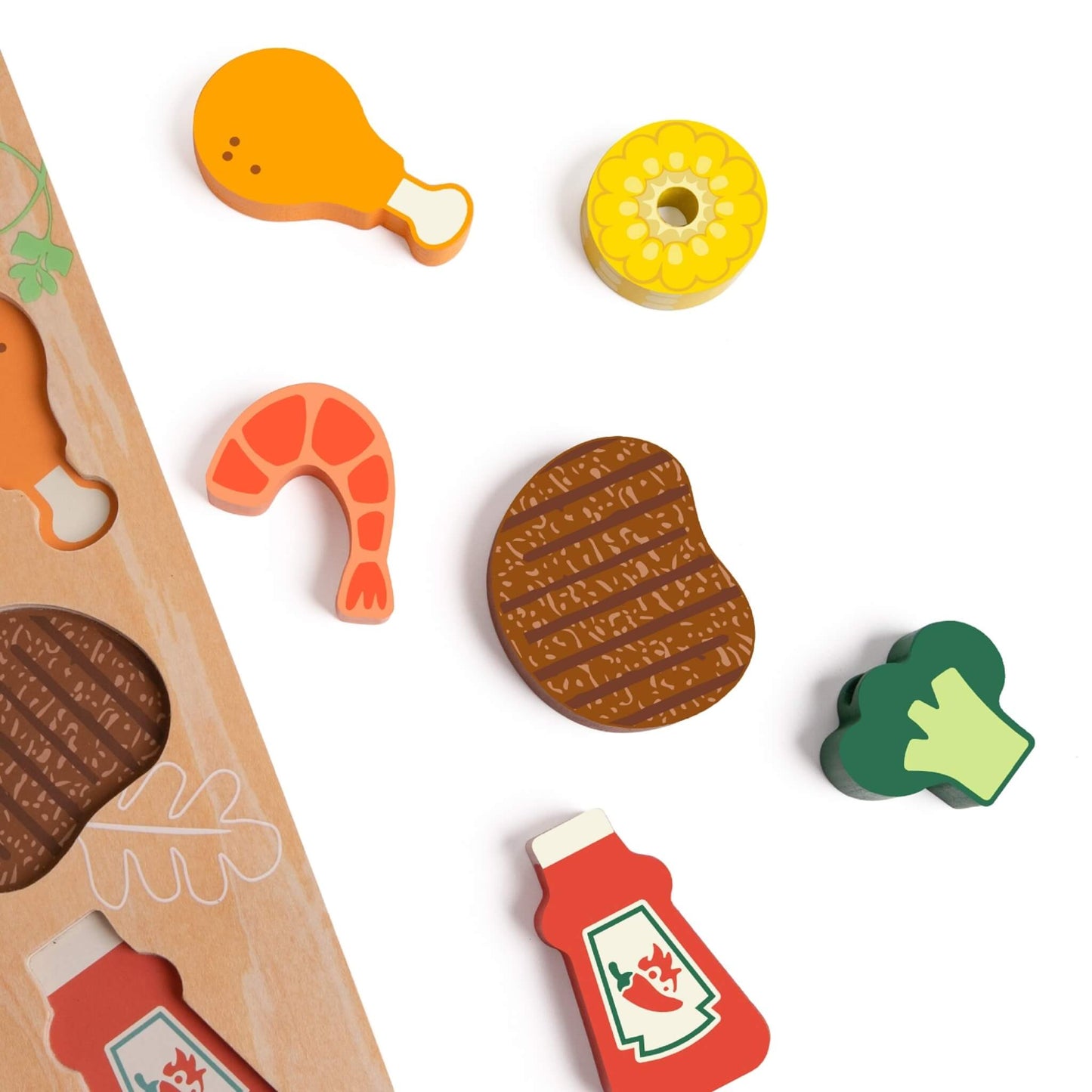 Selection of wooden food pieces including steak, prawn, broccoli, corn and sauce bottle placed beside edge of grill board.