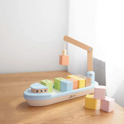 Wooden cargo ship toy on a table with pastel blocks scattered nearby in natural light.