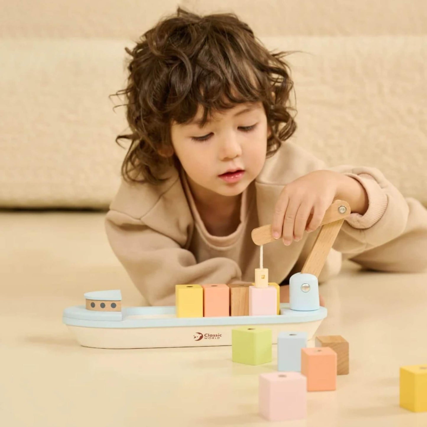 Child lying on the floor, using a wooden block boat  toy to pick up blocks with a crane.