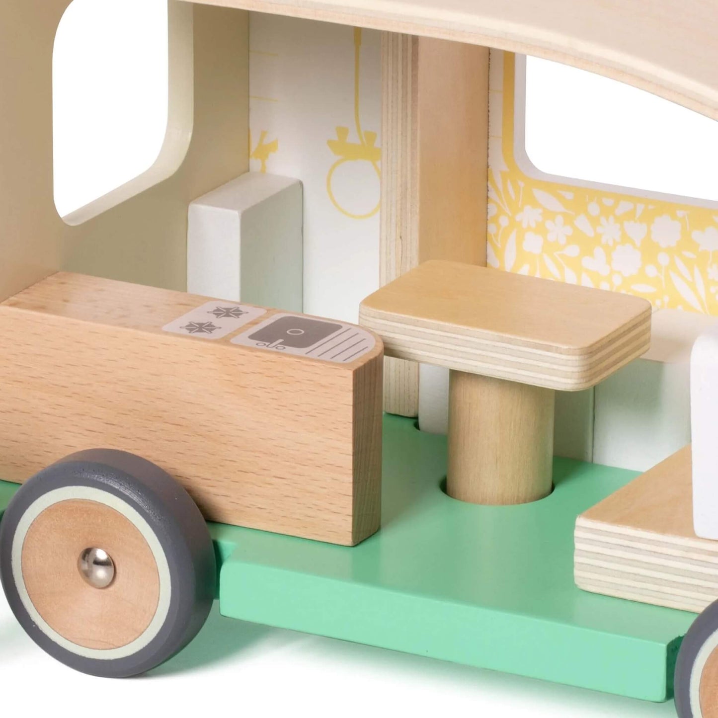 The interior of a wooden toy campervan, showing a small wooden kitchen counter, a table, and bench seats with patterned cushions.