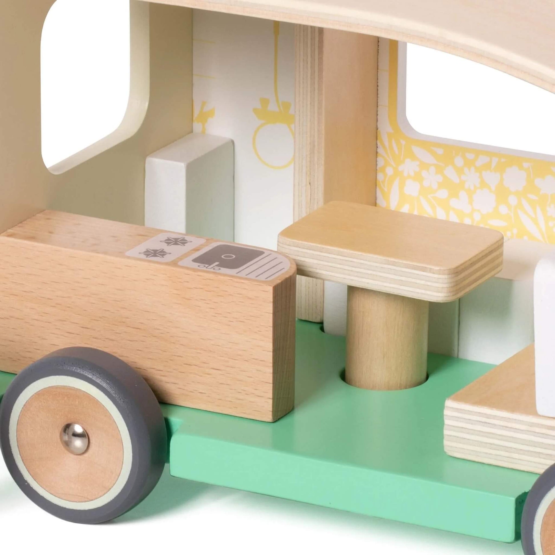 The interior of a wooden toy campervan, showing a small wooden kitchen counter, a table, and bench seats with patterned cushions.