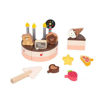 A wooden toy chocolate cake with one slice removed, surrounded by small wooden toppings like a star, strawberry, and heart, plus a wooden cake knife.