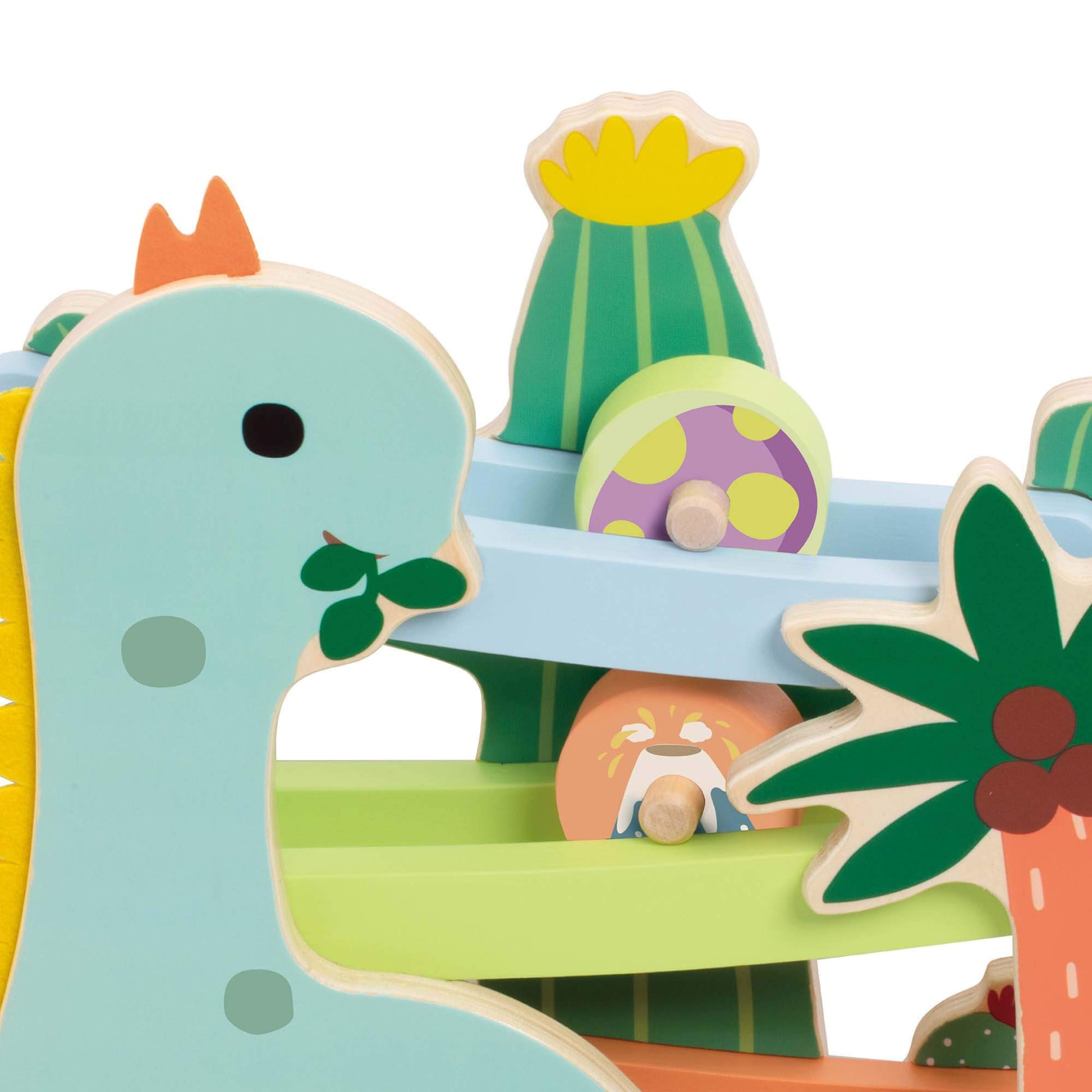 Close-up of a wooden dinosaur ramp toy showing pastel-coloured tracks with wooden discs rolling down, surrounded by painted palm tree and cactus details.